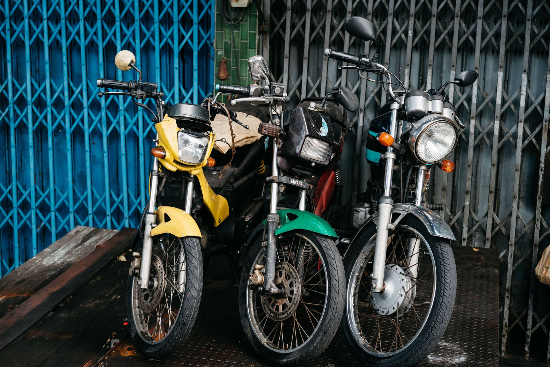 Three parked motorcycles in urban area, vibrant colors and metal grate backdrop.