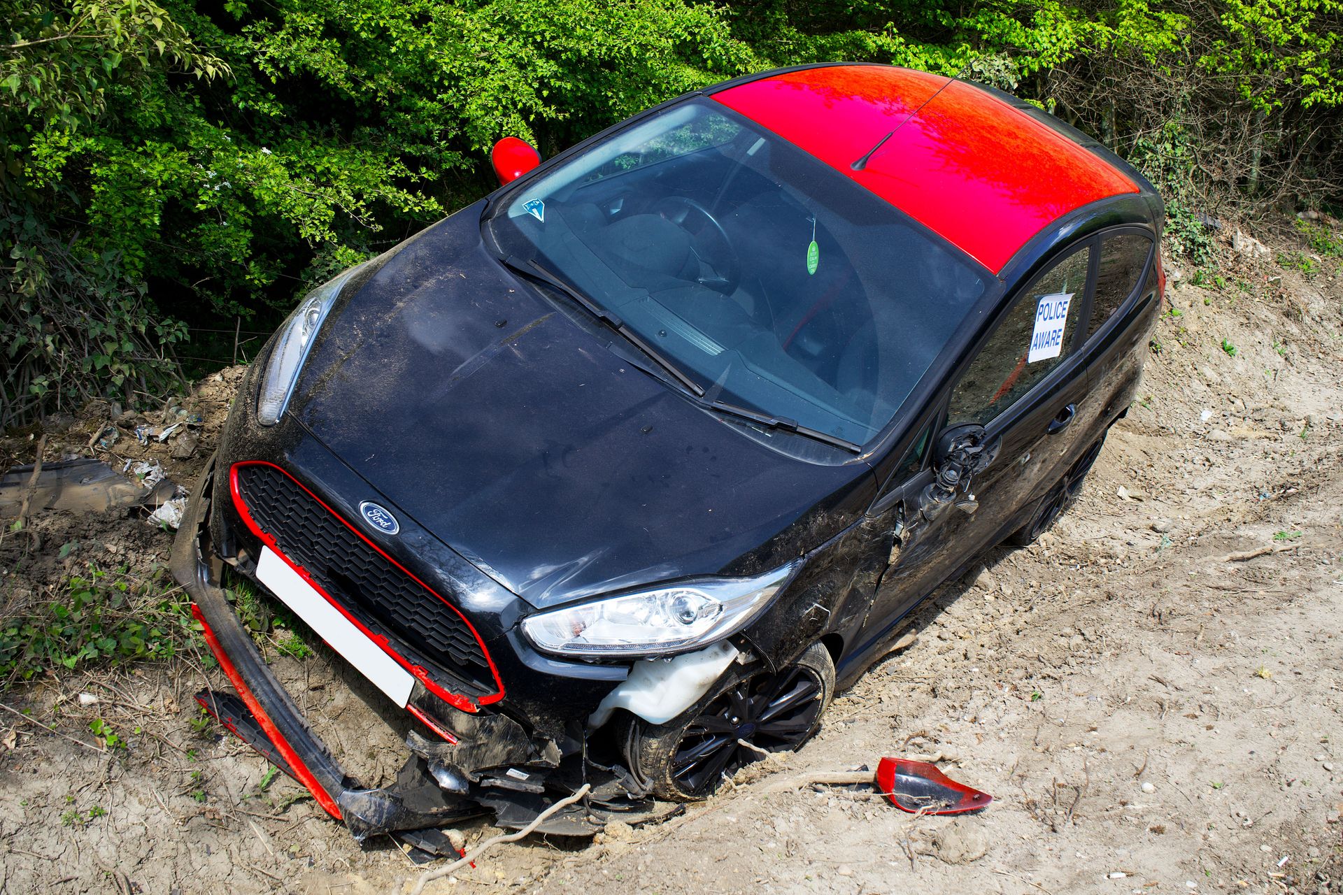 A black and red Ford Fiesta lies abandoned and damaged off-road in Welwyn Garden City, UK.