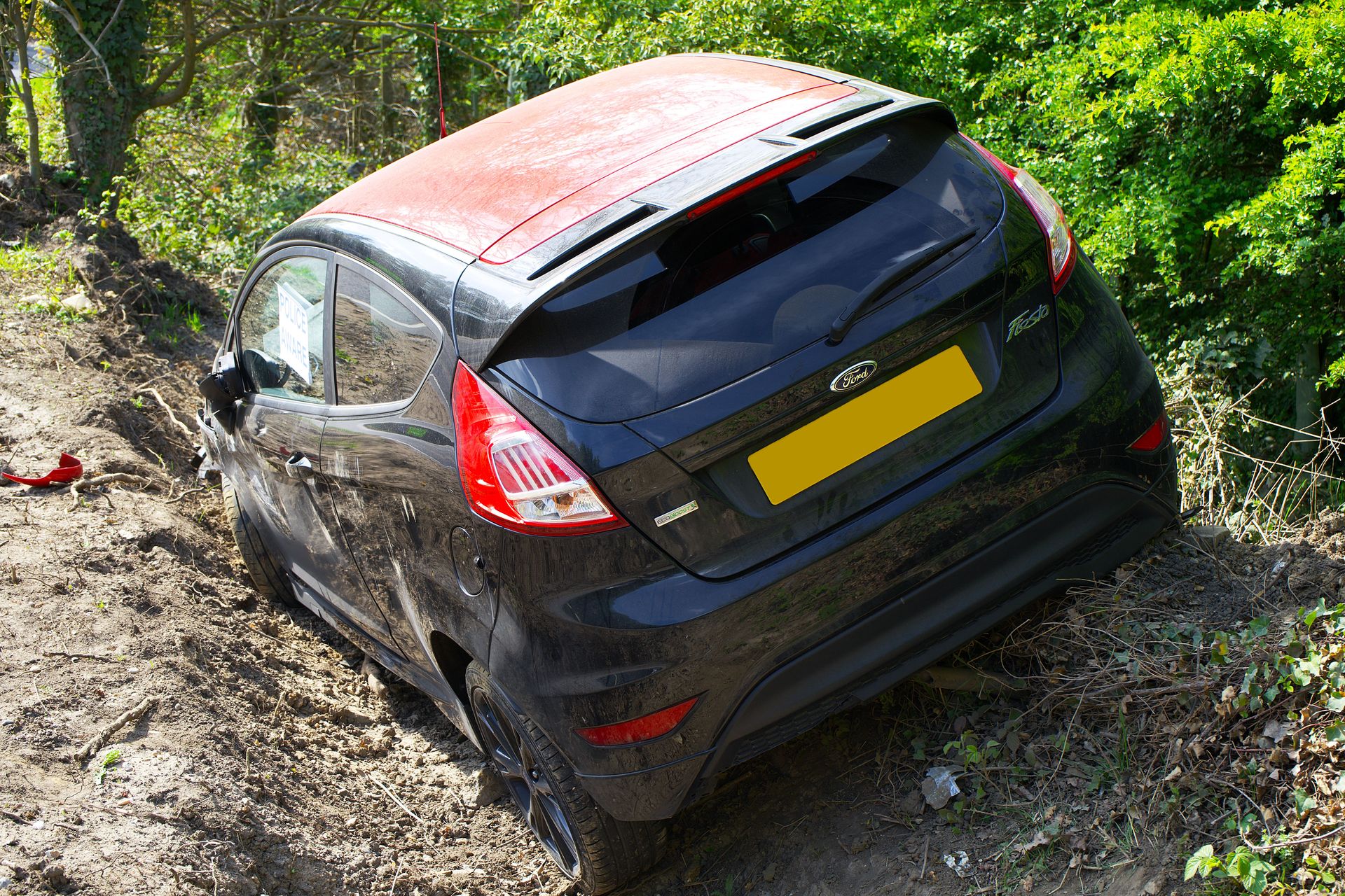 Damaged Ford Fiesta on a dirt roadside, surrounded by green foliage, indicating an accident scene.