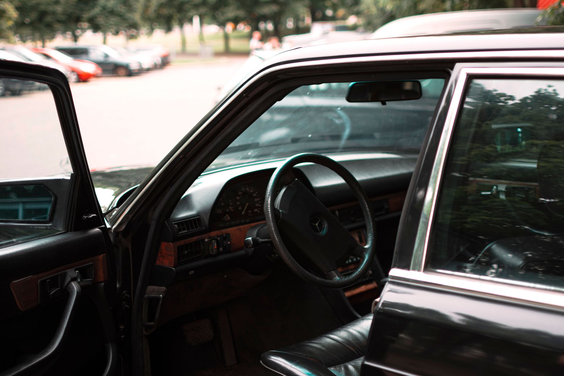 Close-up of an open car door showing the steering wheel and dashboard with a blurred parking lot background.